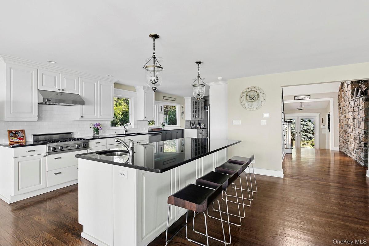 Kitchen with dark wood-style flooring, dark countertops, decorative backsplash, a center island with sink, and under cabinet range hood