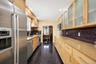 Galley kitchen featuring stainless steel appliances, light wood-finish cabinetry, granite-style countertops, and a dark tile backsplash