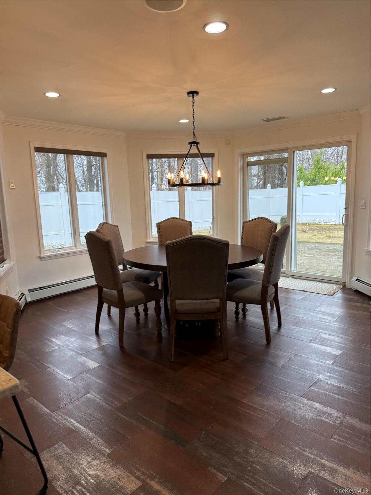 Dining space featuring a notable chandelier, dark wood-style floors, baseboard heating, and ornamental molding