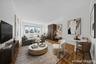 Expansive living space featuring wood-finish parquet flooring, a wide window with cityscape scenery, a built-in wall air conditioning unit, and a dini