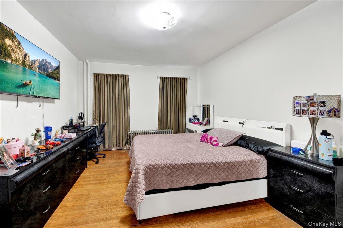 Bedroom featuring an office area, light wood-style flooring, and radiator heating unit
