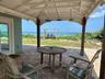 A cozy and shaded outdoor patio with two comfortable chairs and a small table set against a beautiful beachfront.