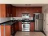 Kitchen with stainless steel appliances, backsplash, range hood, light tile patterned flooring, and dark stone counters
