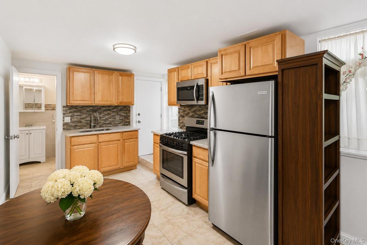 Kitchen featuring wood-finish cabinetry, stainless steel appliances, a mosaic tile backsplash, and light-toned floor tiling