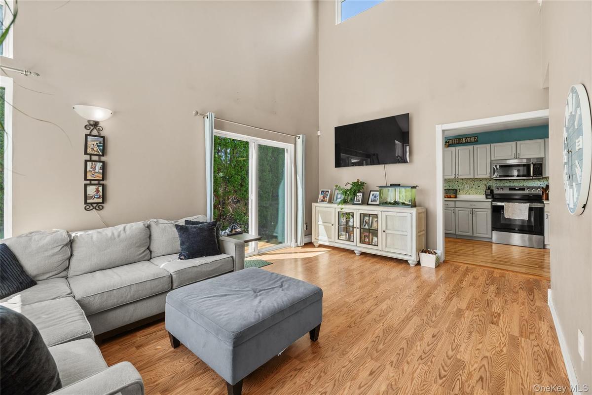 Open-concept living space featuring vaulted ceilings, abundant natural light from sliding glass doors, and wood-finish flooring throughout