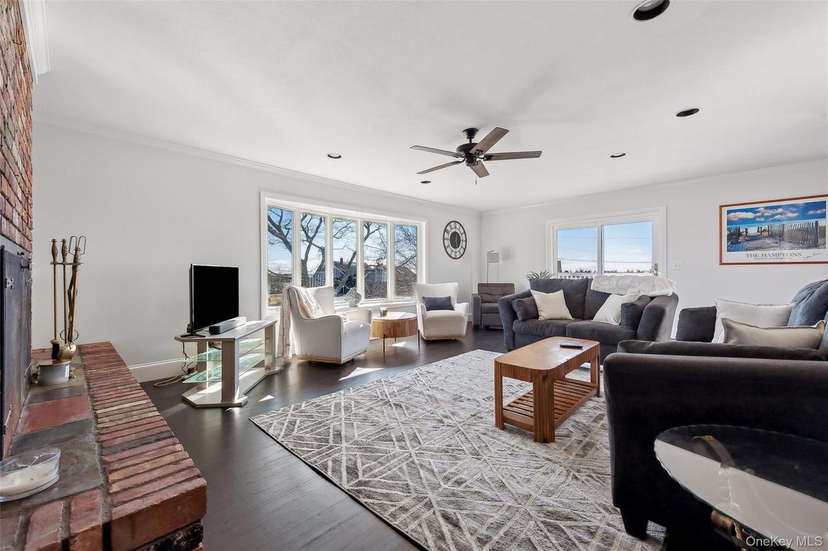 Living room with crown molding, dark wood-type flooring, a fireplace, and ceiling fan