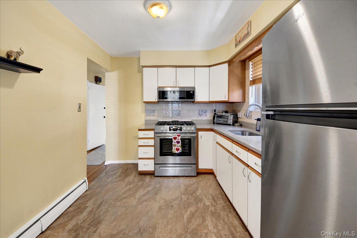 Kitchen featuring stainless steel appliances, off white cabinetry, a single basin sink, light-toned countertops, and patterned backsplash