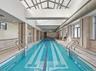 Indoor lap pool with a vaulted glass ceiling, tiled walls, and multiple windows