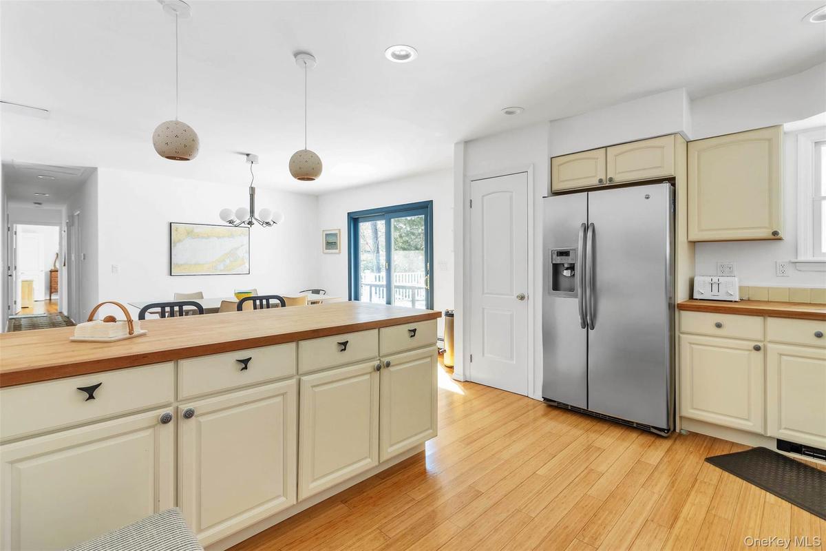 Kitchen with butcher block counters, hanging light fixtures, stainless steel fridge, light hardwood / wood-style floors, and cream cabinets