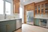 Kitchen with green cabinets, appliances with stainless steel finishes, wine cooler, glass insert cabinets, and light wood-style flooring