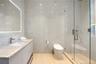 Clean modern en-suite bath featuring full-height white marble tile surround, frameless glass shower with hand-held fixture, smart toilet, floating whi