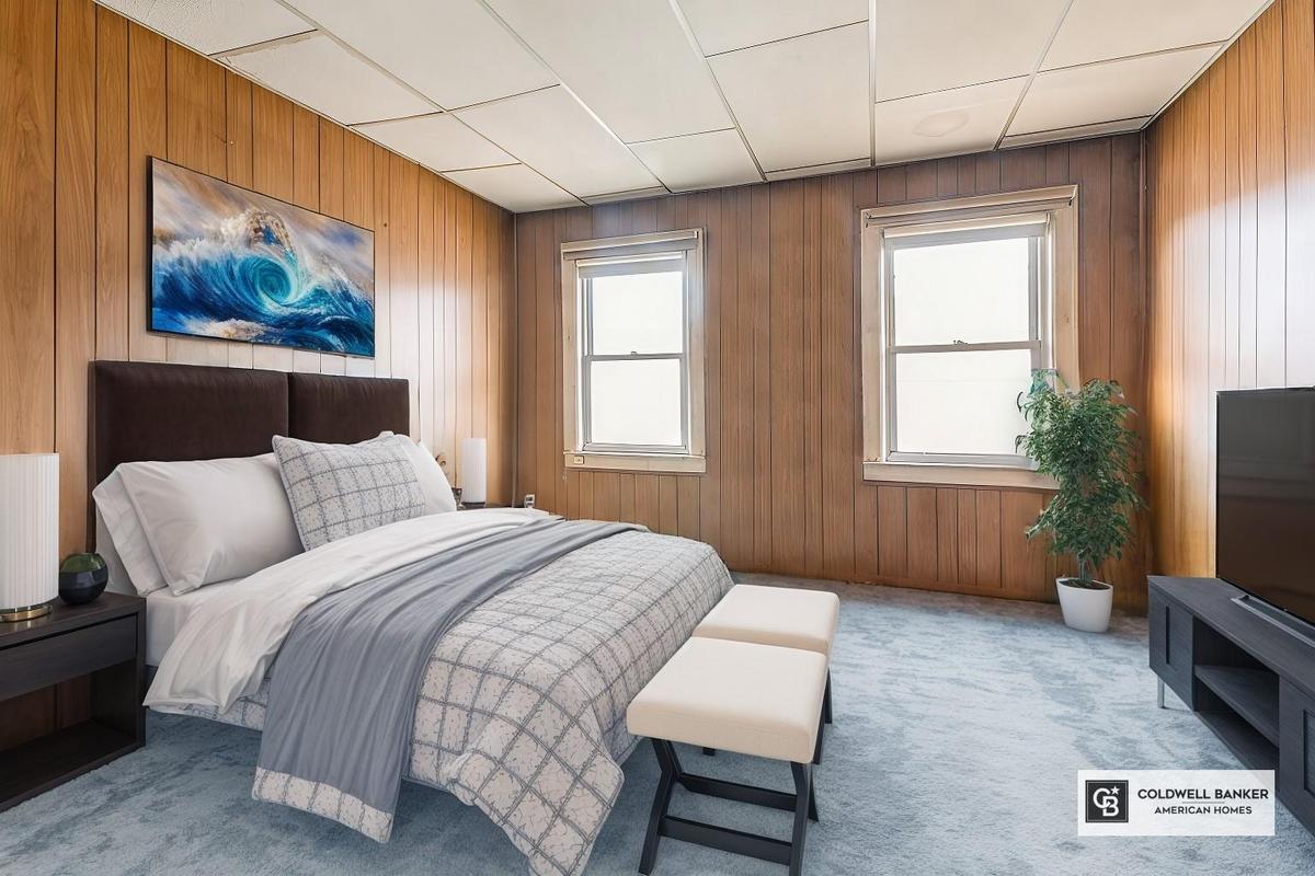 Bedroom with wooden walls, multiple windows, and light colored carpet