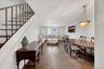 Open-concept living and dining areas featuring wood-finish flooring, a contemporary chandelier with ceiling medallion, and multiple windows providing