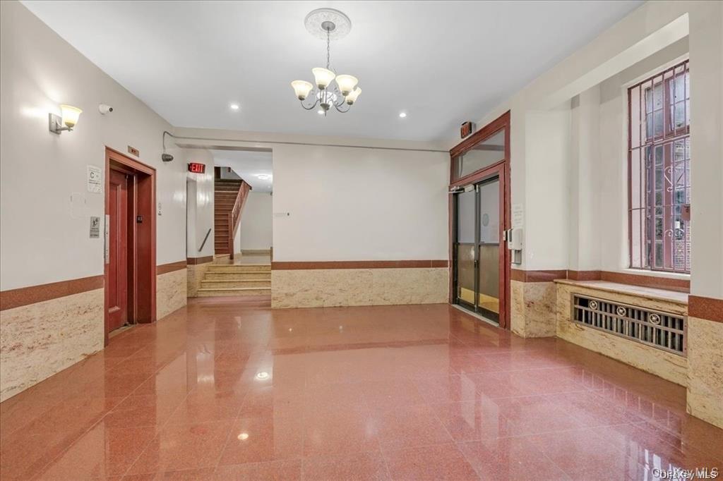 Unfurnished room featuring wainscoting, granite tiled floors, elevator, tile walls, and a chandelier
