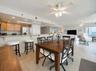 A central dining area connects to the kitchen and living space, all under ceiling fans and surrounded by windows—ideal for casual meals and gatherings