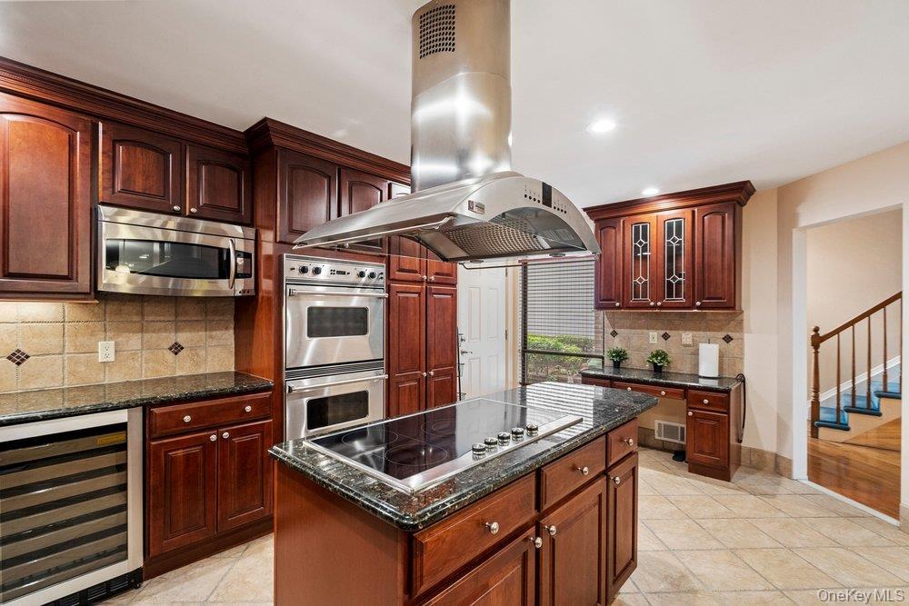 Kitchen featuring a large central island with a built-in cooktop, stainless steel range hood, stainless steel double wall ovens, built-in microwave, a