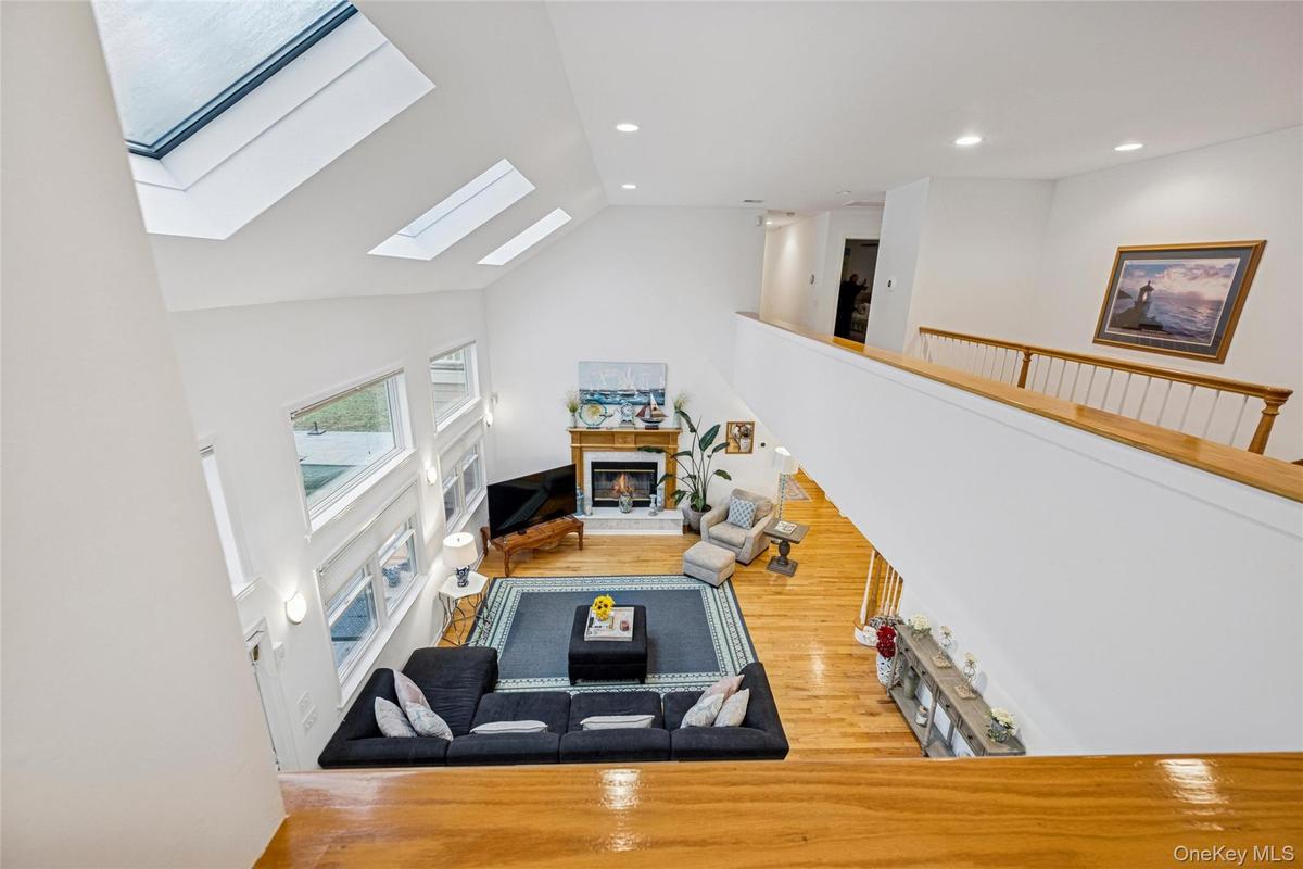 Living area with a glass covered fireplace, a skylight, wood finished floors, recessed lighting, and high vaulted ceiling