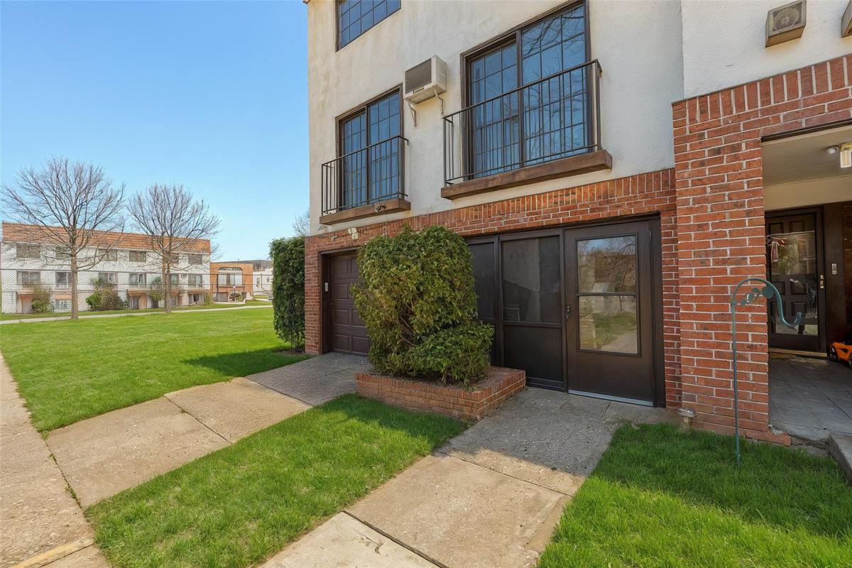 Property entrance with stucco siding, brick siding, a lawn, and a wall unit AC