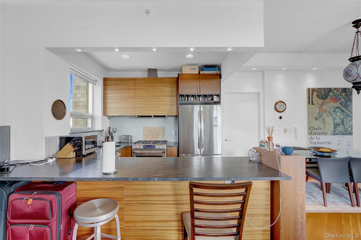 Kitchen featuring dark countertops, stainless steel appliances, a breakfast bar, brown cabinets, and recessed lighting