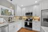 Kitchen with appliances with stainless steel finishes, hanging light fixtures, light stone counters, and white cabinets