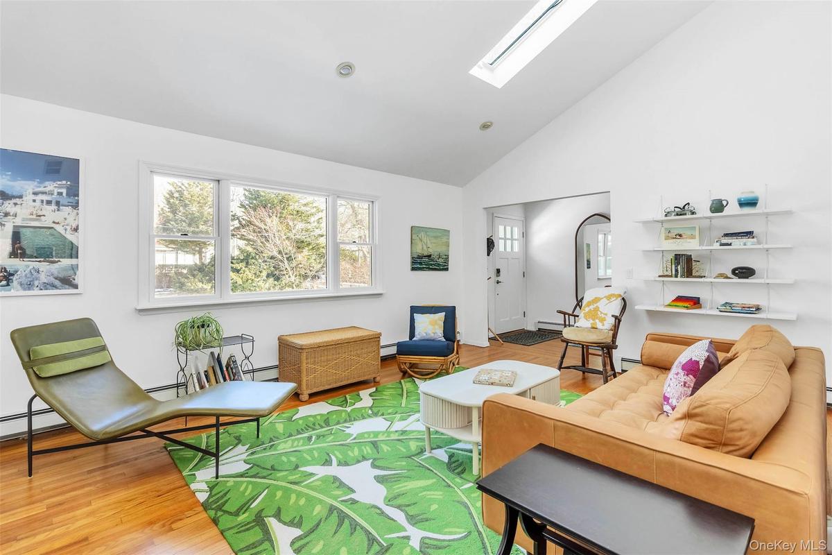 Living room with baseboard heating, high vaulted ceiling, a skylight, and hardwood / wood-style floors