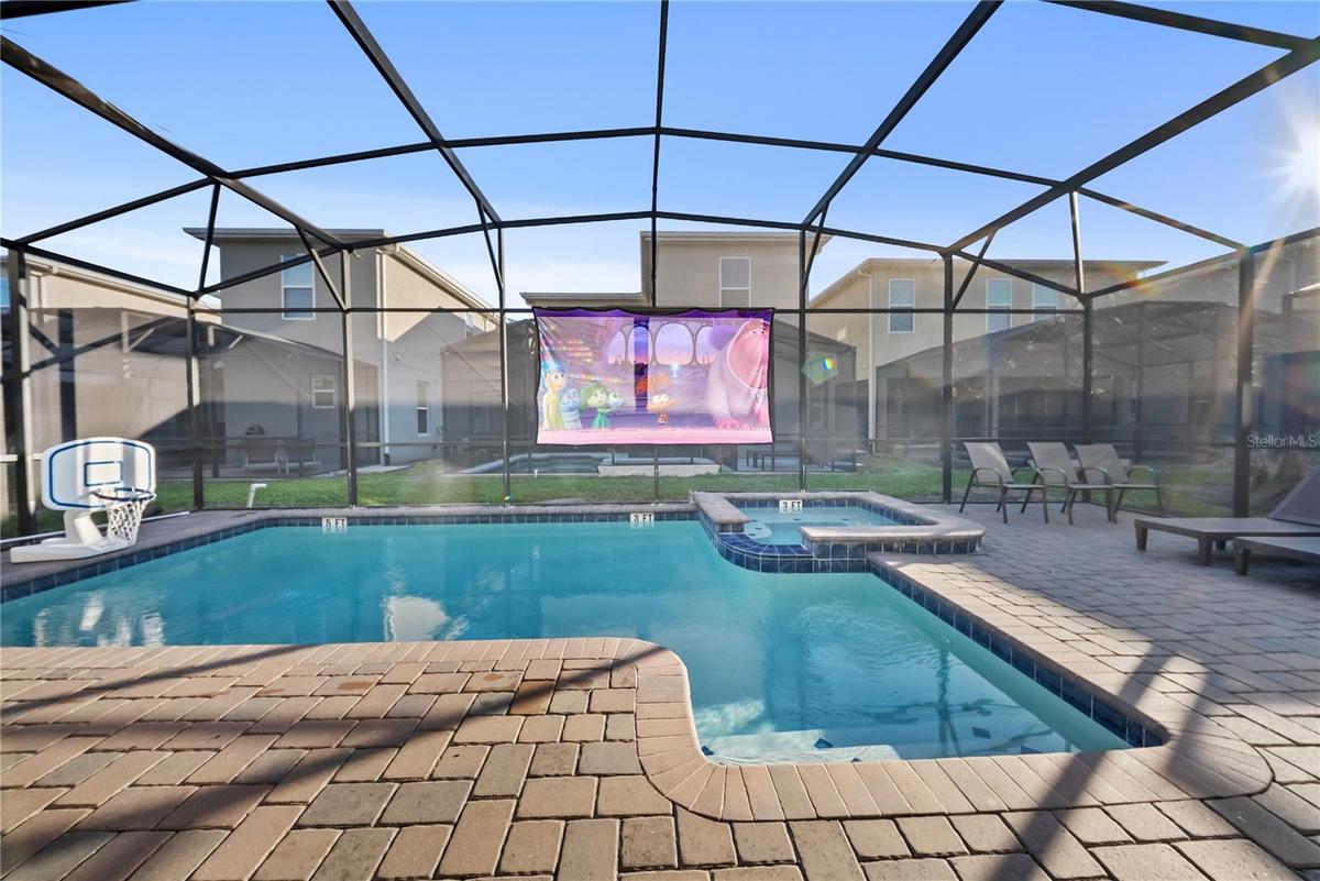 Private screen enclosed pool and hot tub with projector screen, outdoor dining, and lounge area.