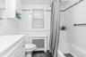 Bathroom featuring white wall tiling with decorative accent borders, a built-in bathtub with shower, a window with blinds, and a vanity with integrate