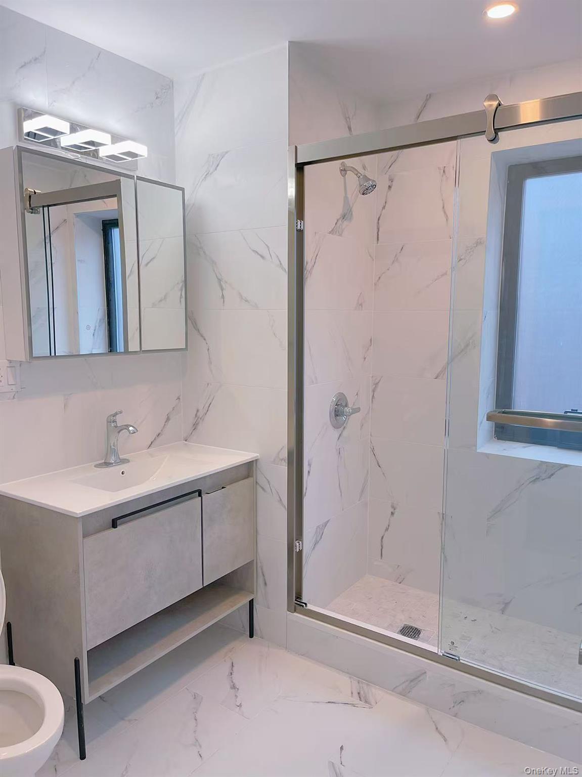 Bathroom featuring marble finish flooring, a marble finish shower, tile walls, and vanity