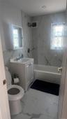 Recently updated bathroom featuring marble-look tile flooring and wall surround, a compact vanity with integrated sink, chrome fixtures, and a tub/sho
