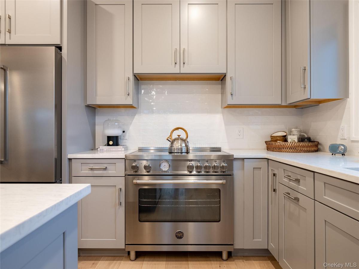 Kitchen with appliances with stainless steel finishes, gray cabinetry, backsplash, and light stone countertops