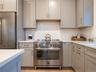Kitchen with appliances with stainless steel finishes, gray cabinetry, backsplash, and light stone countertops