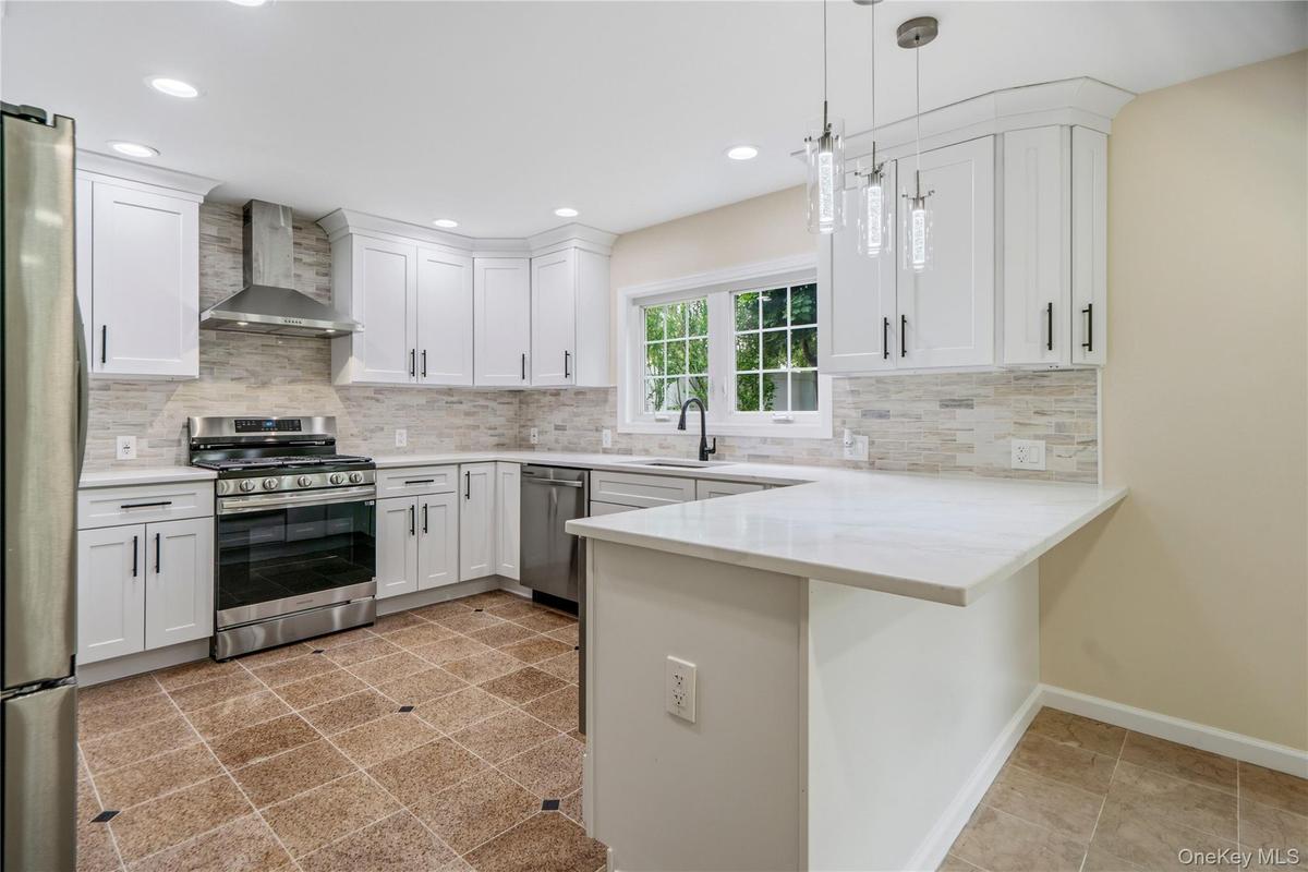 Modern kitchen featuring white shaker cabinetry, stainless steel appliances, light-toned tiled backsplash, and recessed lighting