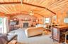 Carpeted living area featuring wooden ceiling, a brick fireplace, wood walls, brick wall, and ceiling fan