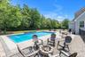 In-ground swimming pool with stone coping, paver patio, stone fire pit, and black fencing