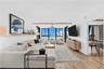 Open-concept living room with sectional seating, swivel lounge chairs, custom wood shelf, and panoramic Tampa Bay views through walls of glass.