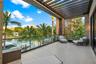 Second-floor waterfront balcony with motorized pergola, frameless glass railing, woven lounge chairs, large-format tile flooring, vertical wood slat s