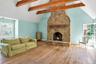 Spacious living area featuring a stone fireplace with a wood mantle, vaulted ceiling with exposed wood beams, wood-finish flooring, and multiple windo