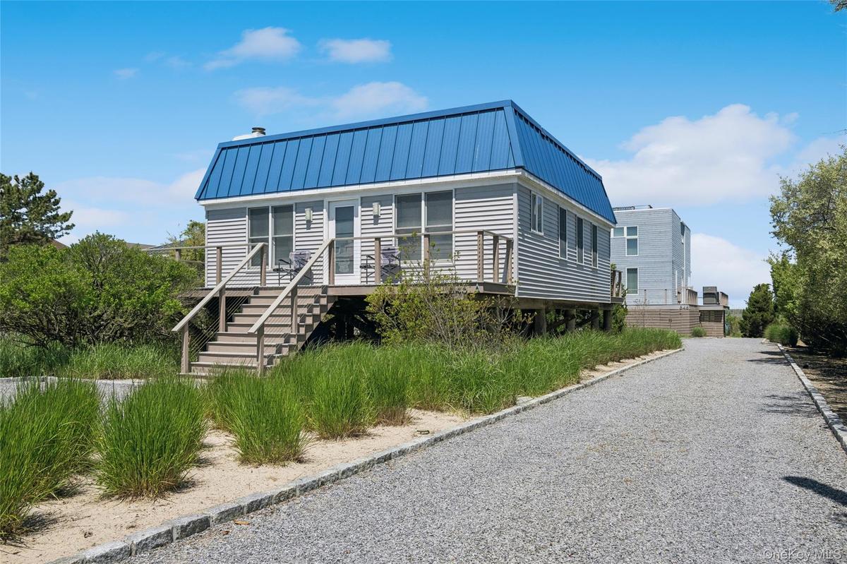 View of front of house featuring a standing seam roof, driveway, stairway, and metal roof