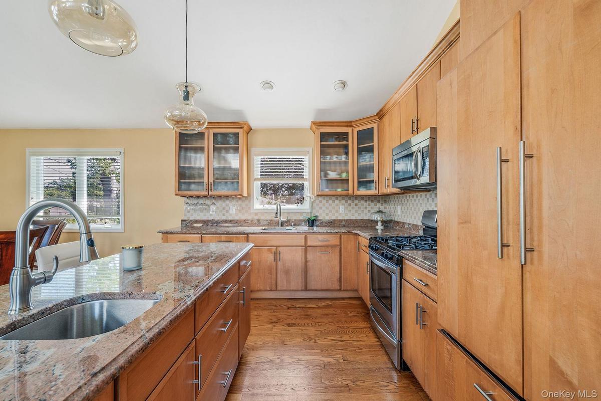 Kitchen with light wood-style floors, appliances with stainless steel finishes, glass insert cabinets, light stone countertops, and decorative light f