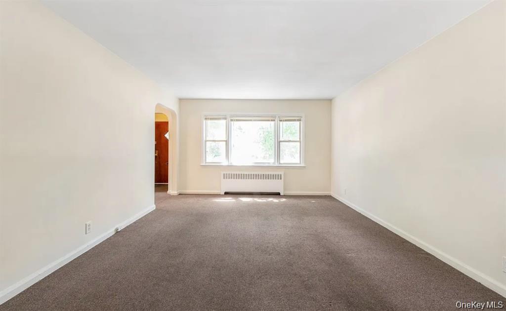 Spare room featuring arched walkways, radiator heating unit, and carpet flooring