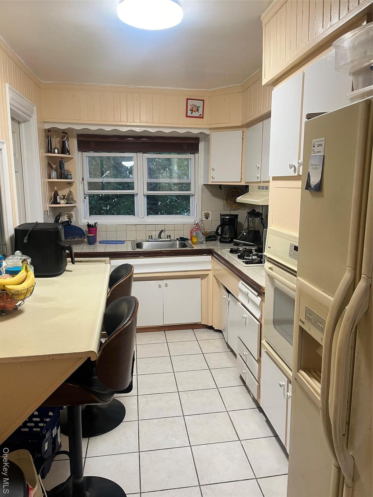 Kitchen with fridge, white cabinets, light tile patterned floors, wall oven, and backsplash