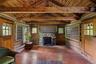 Rustic cabin interior with exposed log walls, hand-hewn beams, and a stone, wood-burning fireplace