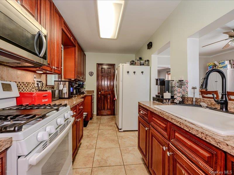 Galley kitchen featuring wood-finish cabinetry, stone-look countertops, and tile flooring