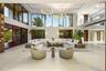 Grand double-height living room with wraparound sectional seating, light stone floors, dual ring chandelier, full-wall glass overlooking tropical wate
