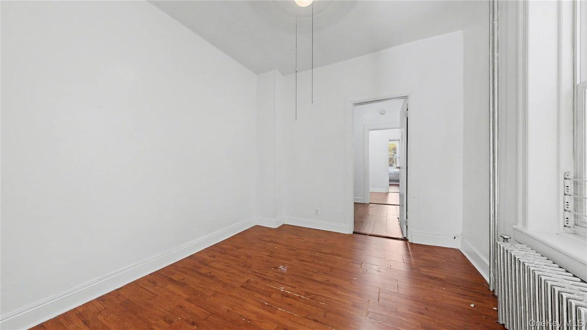 Unfurnished bedroom featuring radiator heating unit and dark wood-style floors
