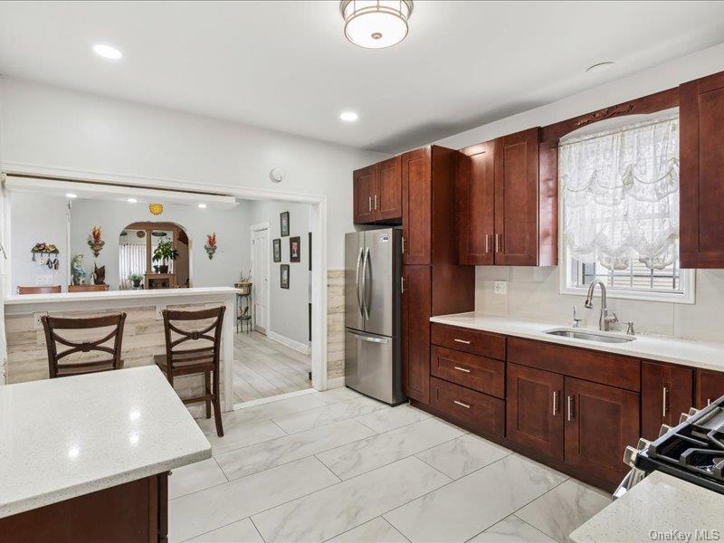 Kitchen featuring freestanding refrigerator, light finish flooring, gas range oven, backsplash, and dark wood finish cabinets