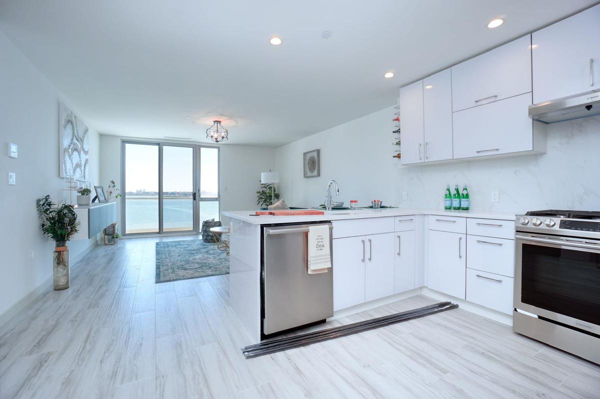 Kitchen featuring a peninsula, white cabinets, under cabinet range hood, light countertops, and stainless steel appliances
