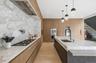 Kitchen with modern cabinets, light stone counters, decorative light fixtures, appliances with stainless steel finishes, and wall chimney exhaust hood