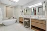 Luxurious primary bath featuring custom vanities, marble floors, walls and shower and lavish freestanding soaking tub.