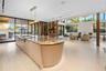Wide-angle view of open-plan kitchen and great room with curved fluted island, book-matched stone countertop, brass cooktop fixtures, full-height illu